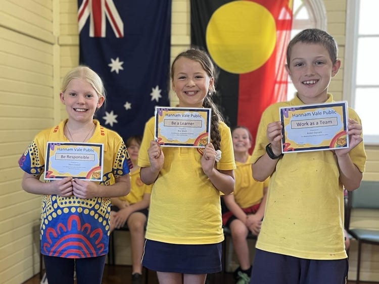 A photo of students holding award certificates at a school assembly.